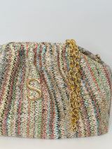 Nahaufnahme der Bucket Bag mit abnehmbarer goldenen Schulterkette. Die Tasche ist in einem vertikalen Strickmuster in zarten Farbtönen Gelb, Hellblau, Rostrot, Grün, Schwarz, Beige. Die Tasche ist zum aufklappen und kann auch als Kulturbeutel genutzt werden. Goldenes Logo platziert in der Mitte der Tasche.