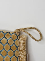 Nahaufnahme der der Handschlaufe der beige-goldene Clutch mit geometrischem Muster aus samtigen Fransen-Tupfen auf hellblauem Grund. Die Tasche hat einen goldfarbenen Reißverschluss mit Quaste, eine kleine Label-Plakette mit „SORENA“, und eine feine Fransenbordüre; innen goldfarben gefüttert. Eine abnehmbare, goldfarbene Kette sorgt dafür, dass man die Tasche auch als Schultertasche tragen kann.