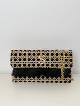 Rechteckige Clutch in schwarz/beige aus handgemachtem, texturiertem Stoff mit edlem gleichmäßigen Punkt Muster und Fransen an der Umschlagklappe. Eine goldfarbene Kette sorgt dafür, dass man die Tasche auch über die Schulter tragen kann. In der Mitte vorne befindet sich das Logo "S" für Soren in Gold. Die Clutch ist vor einem neutralen Hintergrund fotografiert.