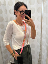 Crossbody Handykette mit grafischem Muster in Pink, Orange und Rosa Farbtönen gezeigt von einer Frau in einem weissen Sweater und olivegrünem Rock.