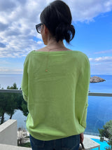 Limettenfarbener Cashmere-Poncho ‚ALTHEA‘ mit weitem U-Boot-Ausschnitt und schmalen Ärmeln, locker fallend, fotografierte Rückenansicht, im Hintergrund sieht mas das Meer.