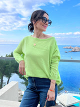 Limettenfarbener Cashmere-Poncho ‚ALTHEA‘ mit weitem U-Boot-Ausschnitt und schmalen Ärmeln, locker fallend, im Hintergrund sieht mas das Meer.