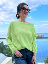 Limettenfarbener Cashmere-Poncho ‚ALTHEA‘ mit weitem U-Boot-Ausschnitt und schmalen Ärmeln, locker fallend, im Hintergrund sieht mas das Meer.