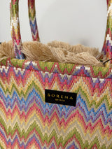 Detailfoto der handgefertigten Medium‑Tote im Zick Zack Muster in der Farbe Ivory/Beige/BLau/Lila/Grün/Gelb/Rosa aus gewebtem Stoff mit seidiger Haptik, etwa 20×17 cm. Sie hat kurze Stoffgriffe, innen rotes Samtfutter, einer abnehmbaren Schulterkette, Magnetverschluss und dekorative Fransenkante.