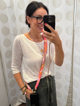 Crossbody Handykette mit grafischem Muster in Pink, Orange und Rosa Farbtönen gezeigt von einer Frau in einem weissen Sweater und olivegrünem Rock.